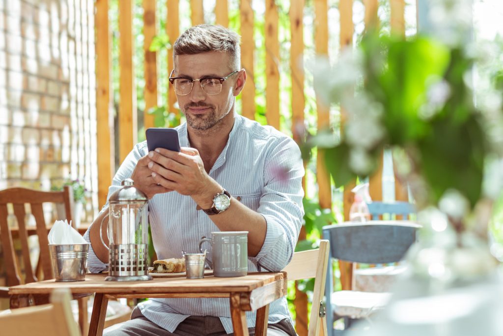 Happy guy ordering with his phone at a table-min Trivec Buddy